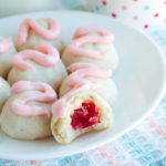 Cookies with pink frosting and cherry in the middle on a plate.