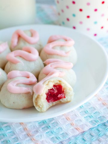 Cookies with pink frosting and cherry in the middle on a plate.