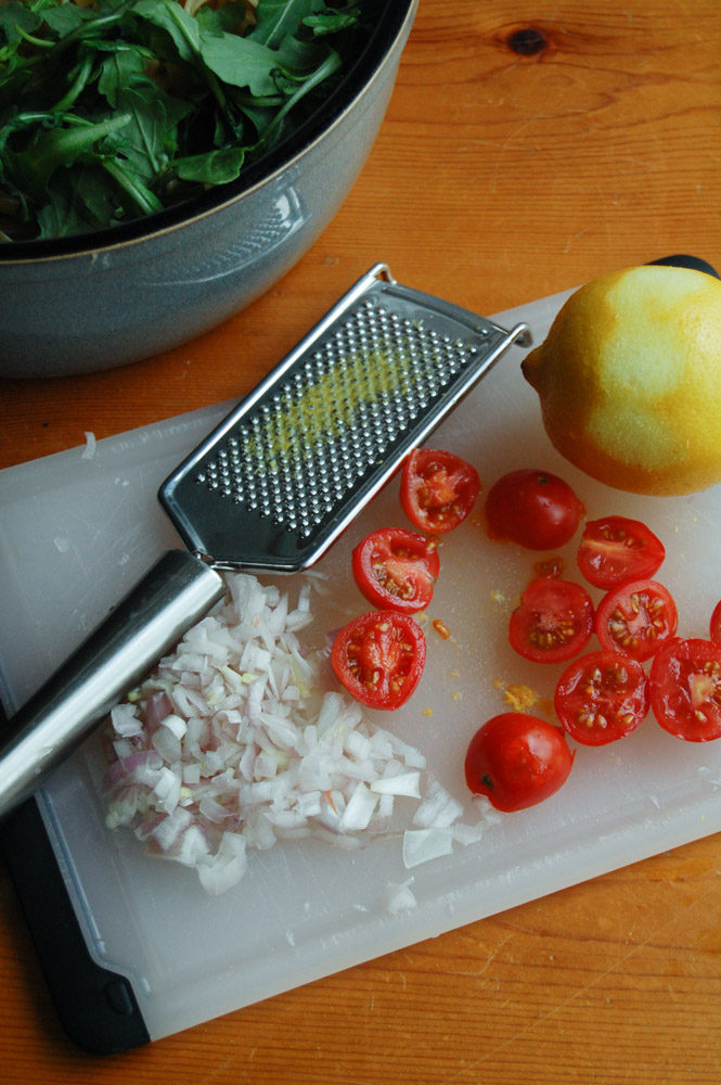 Bowl of arugala, lemon zest, diced tomatoes and shallots on a cutting board