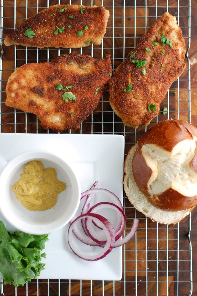 chicken schnitzel with a bowl of mustard, onion and pretzel bun