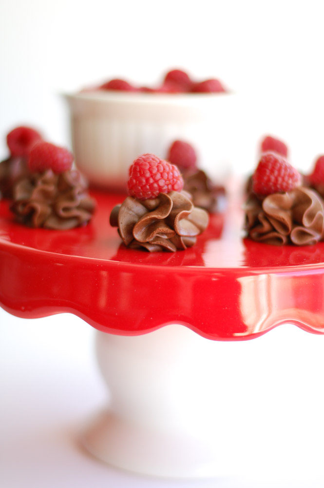 Red cake stand with chocolate raspberry truffles and a bowl of raspberries
