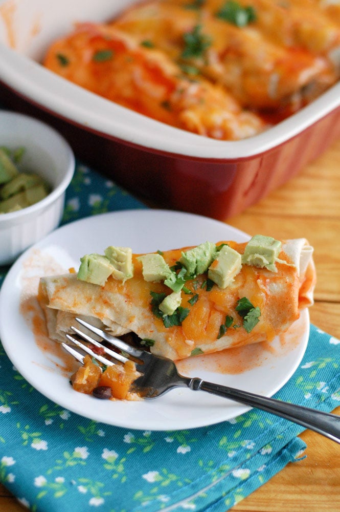 plate with a butternut squash enchilada with a fork and casserole dish in background