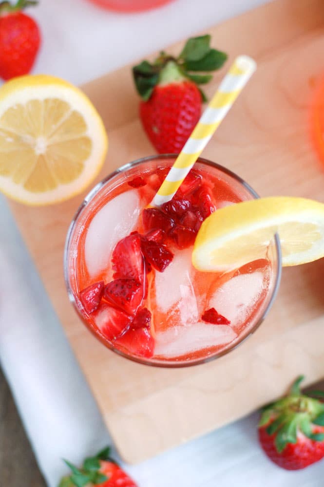 Top view of glass with strawberry lemonade and strawberries and lemon beside the glass. 