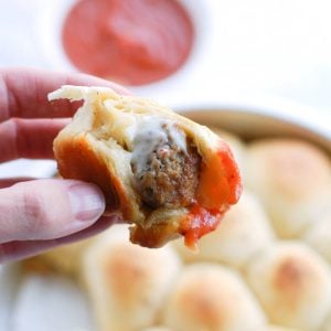 Hand holding meatball wrapped in bread and sauce.