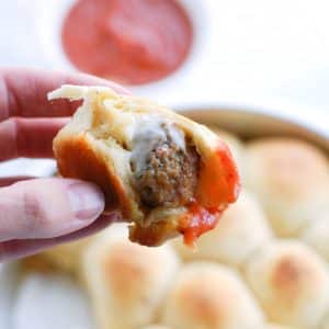 Hand holding meatball wrapped in bread and sauce.