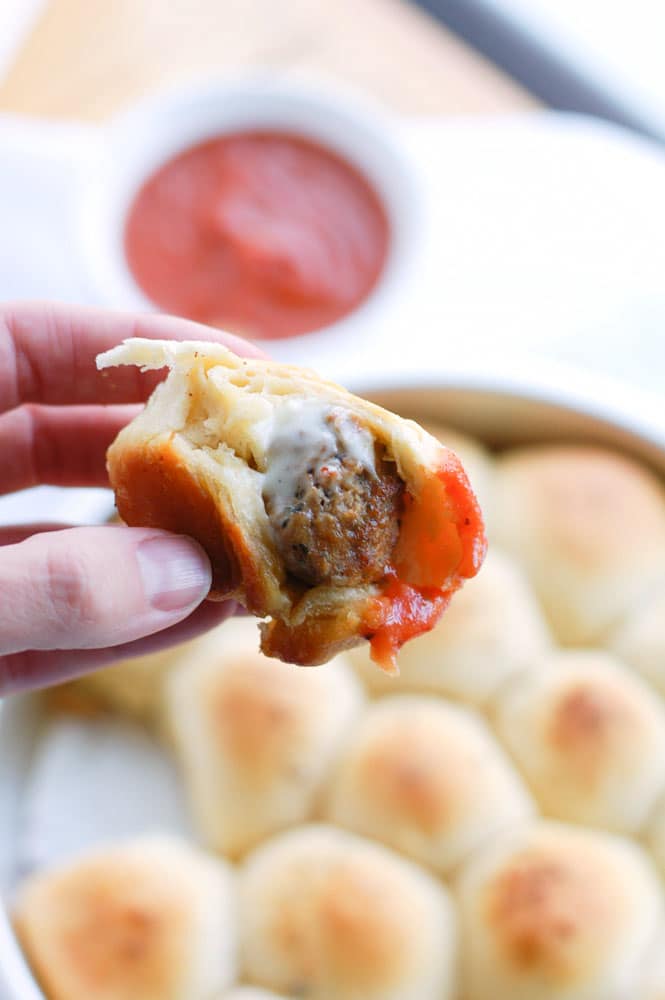 Meatball biscuit bombs Hand holding meatball wrapped in bread and sauce.