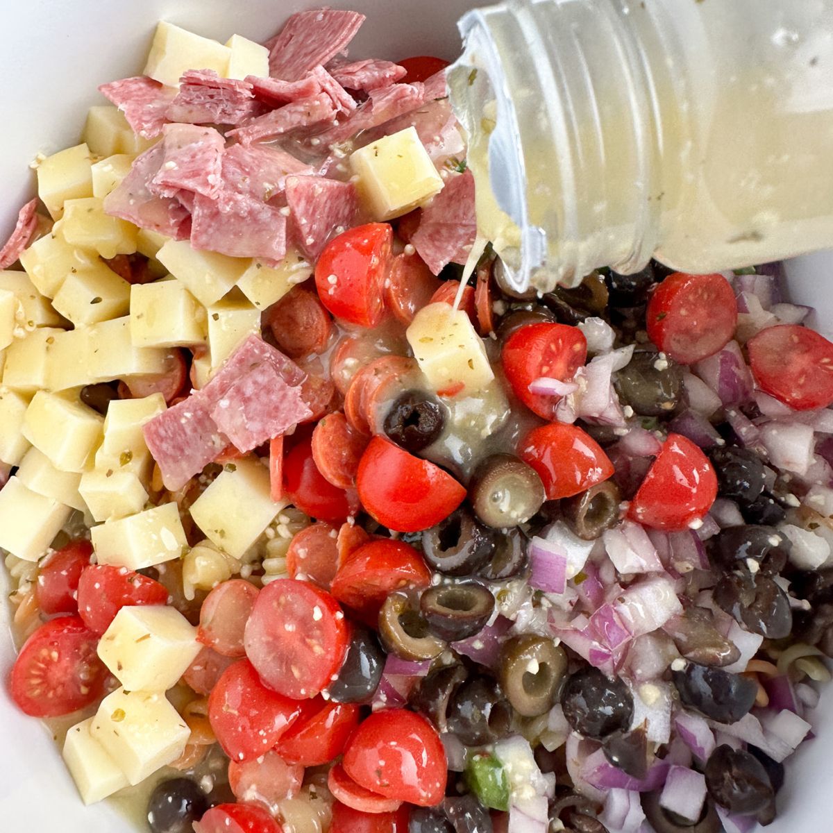Bowl with diced cheese, salami, olives, tomatoes, and dressing. 