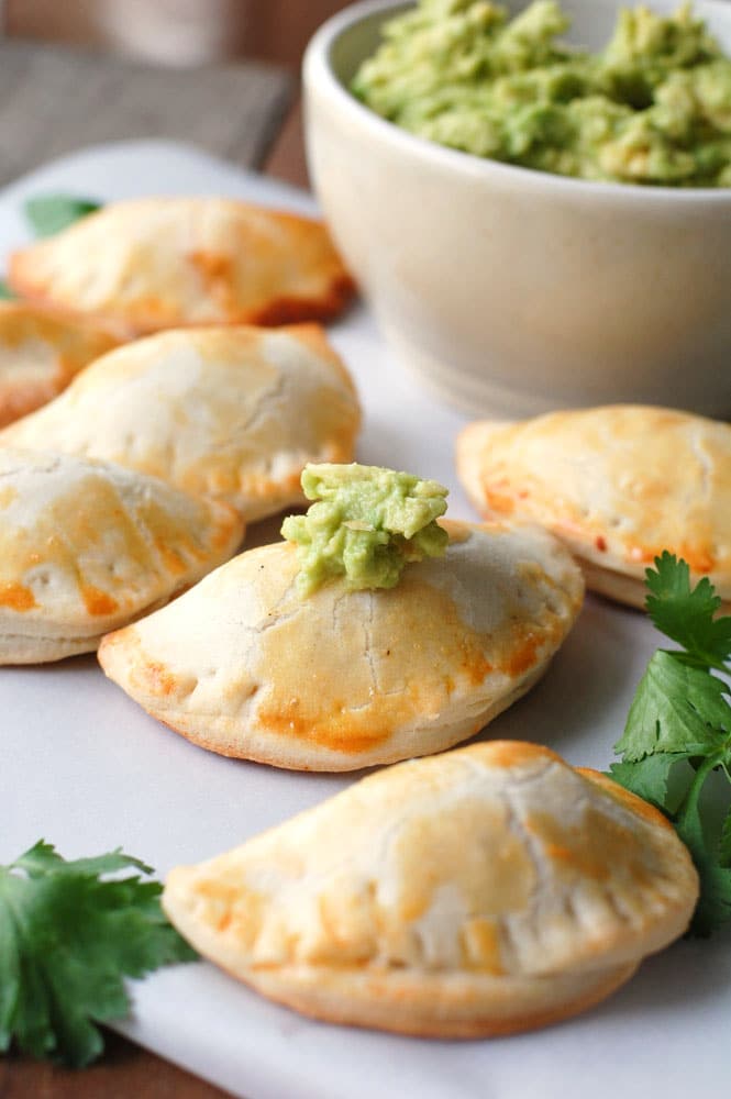 Several empanadas on a table with guacamole. 