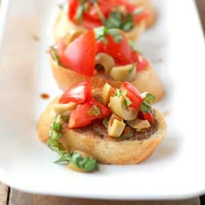 Pieces of bread with green olives and tomatoes.