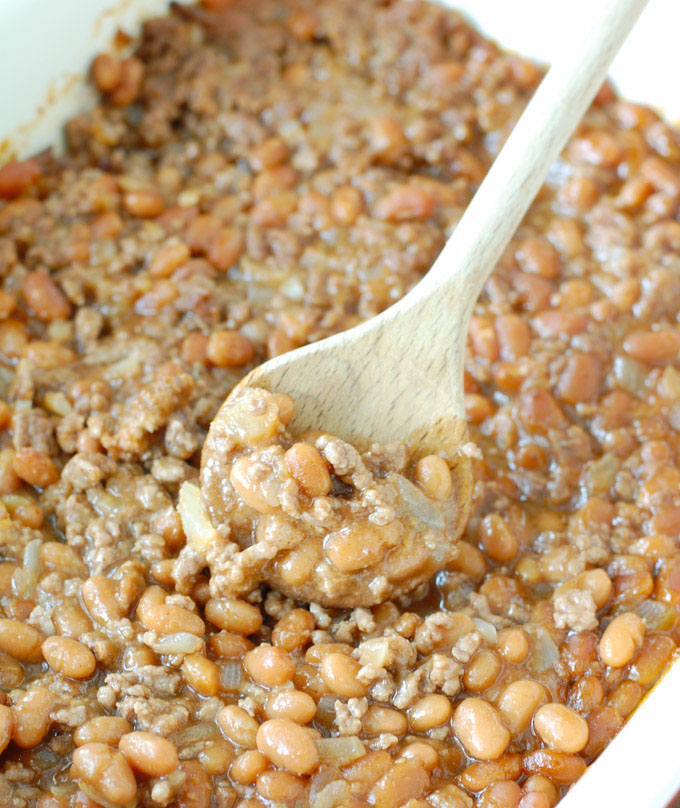 homemade baked beans in a casserole dish with a wooden spoon