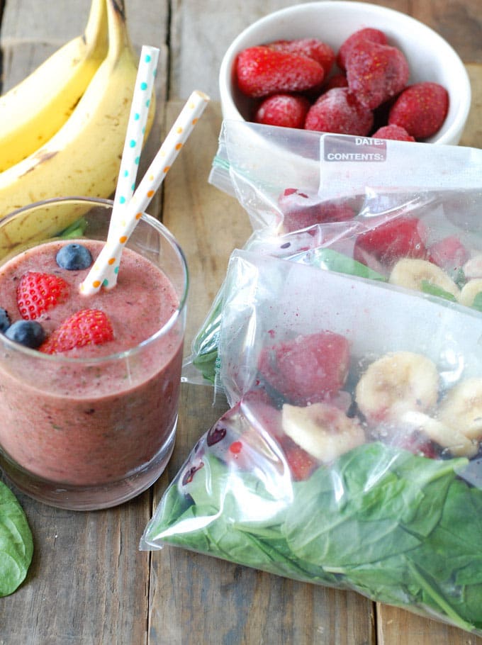 Glass of smoothie with bags of frozen spinach, banana, strawberry and blueberries