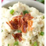 Bowl of mashed potatoes topped with bacon and green onions.