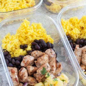 Container with chicken, black beans, yellow rice and pineapple.