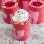 Red and pink candy shot glasses filled with whipped cream.