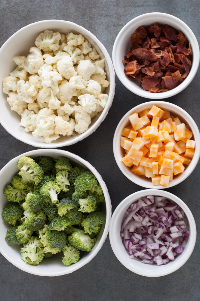 Bowl of broccoli, cauliflower, bacon, cheese cubes and red onion