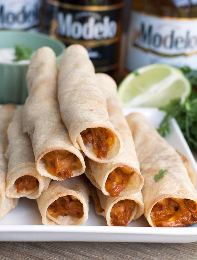 BBQ taquitos stacked on a plate with a lime