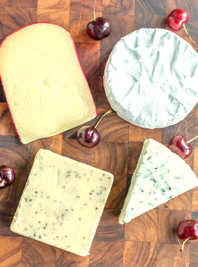 Four different cheeses on a cutting board with cherries
