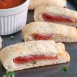 Sliced stromboli on baking dish with bowl of sauce.