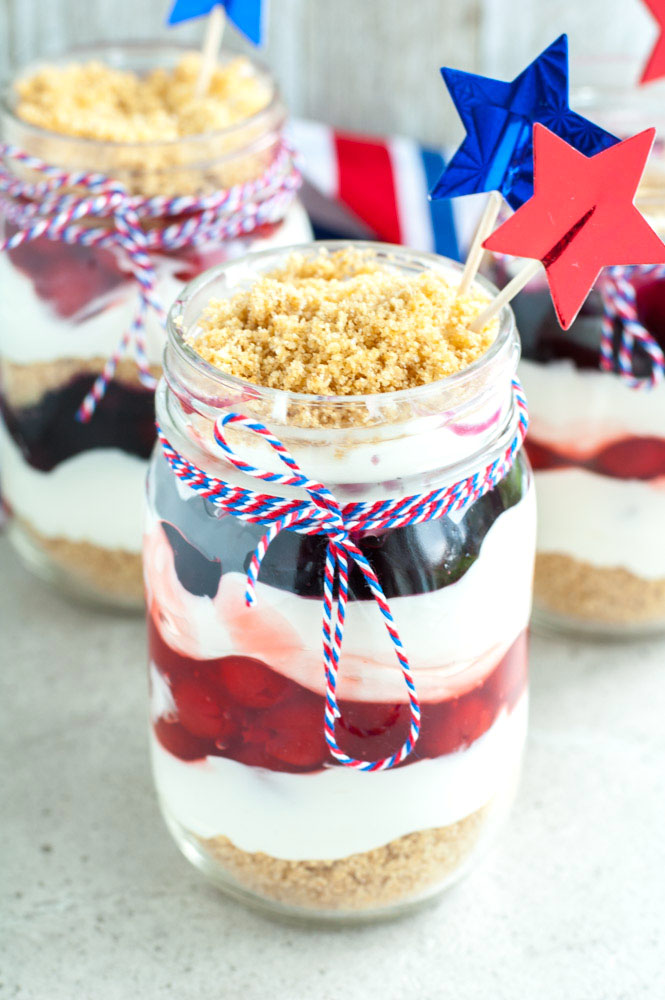 Mason jar with cherry and blueberry trifle wrapped in red, white and blue string. 