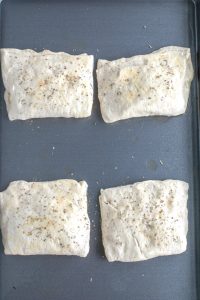 Folded dough with Italian spices on top laying on a sheet pan