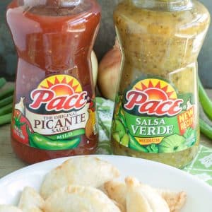 Bottles of salsa on table with bowl of empanadas.