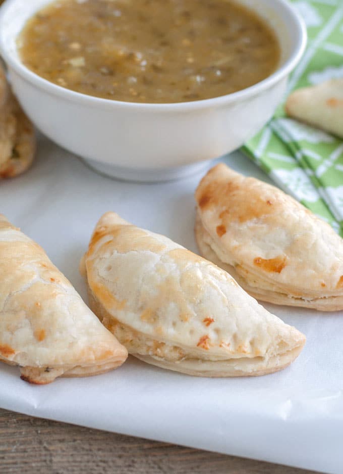 salsa verde empanadas on parchment paper and a bowl of salsa verde