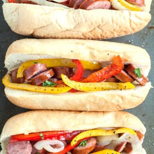 Hot dog bun filled with sausages, peppers, onion.