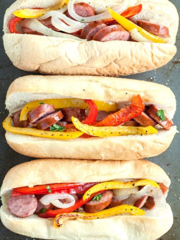 Hot dog bun filled with sausages, peppers, onion.