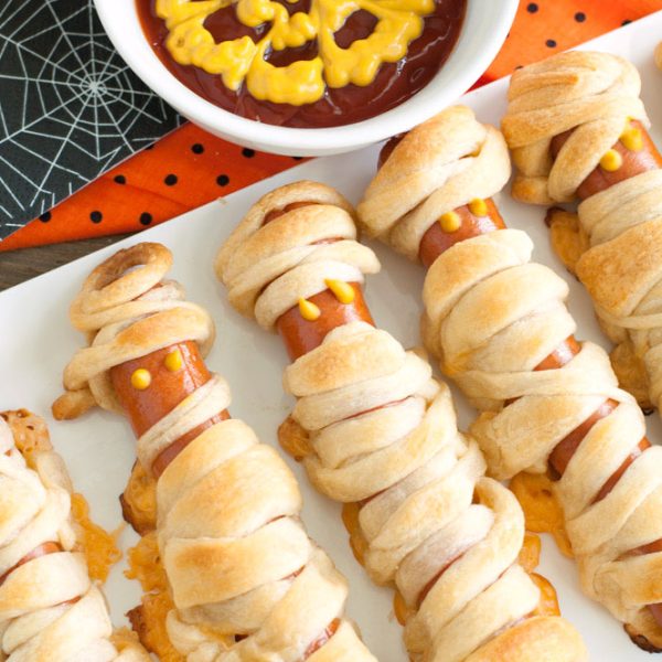 Hot dogs wrapped in crescent rolls with bowl of ketchup and mustard.