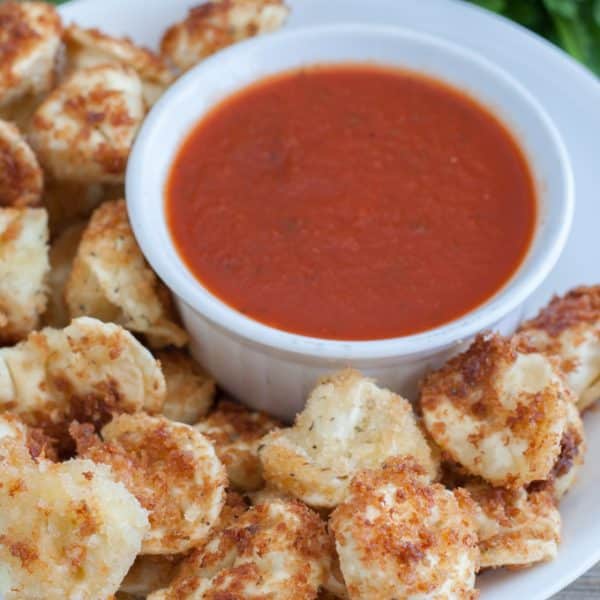 Fried tortellini in bowl with bowl of sauce.