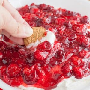 Hand holding cookie dipping in cherry dip.