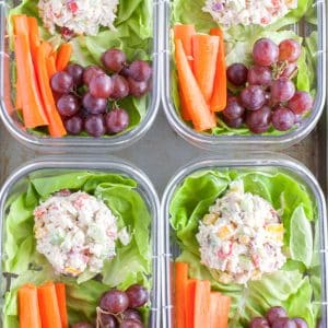 Containers with chicken salad, carrots and grapes.