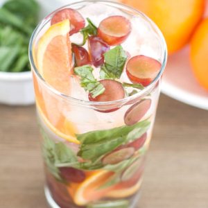 Glass of water with oranges, grapes and basil.