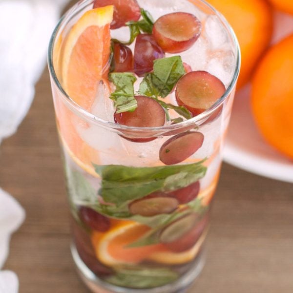 Glass of water with oranges, grapes and basil.