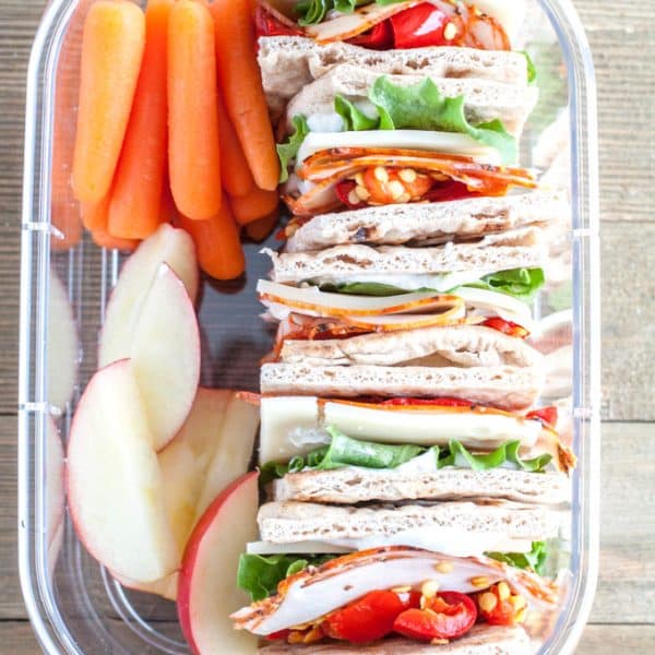 Container with stacked sandwich carrot stacks and apple slices.