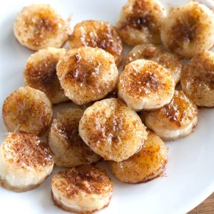 Cooked, sliced bananas with brown sugar on plate.