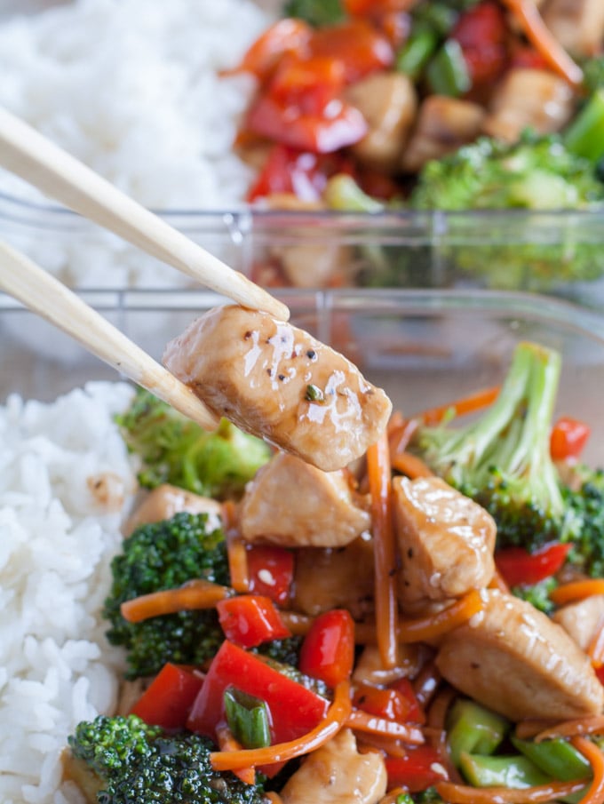Chopsticks holding chicken with broccoli and peppers. 