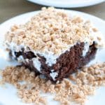 Piece of chocolate cake topped with icing and toffee bits.