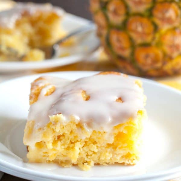 Piece of yellow cake with icing and pineapple in background.