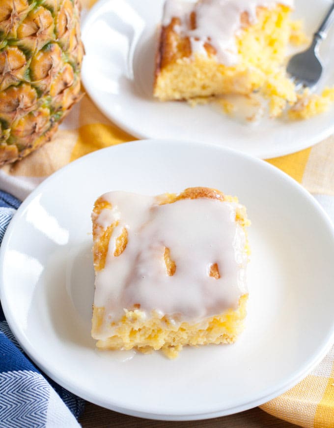 One pieces of pineapple cake on a white plate with a pineapple in the background