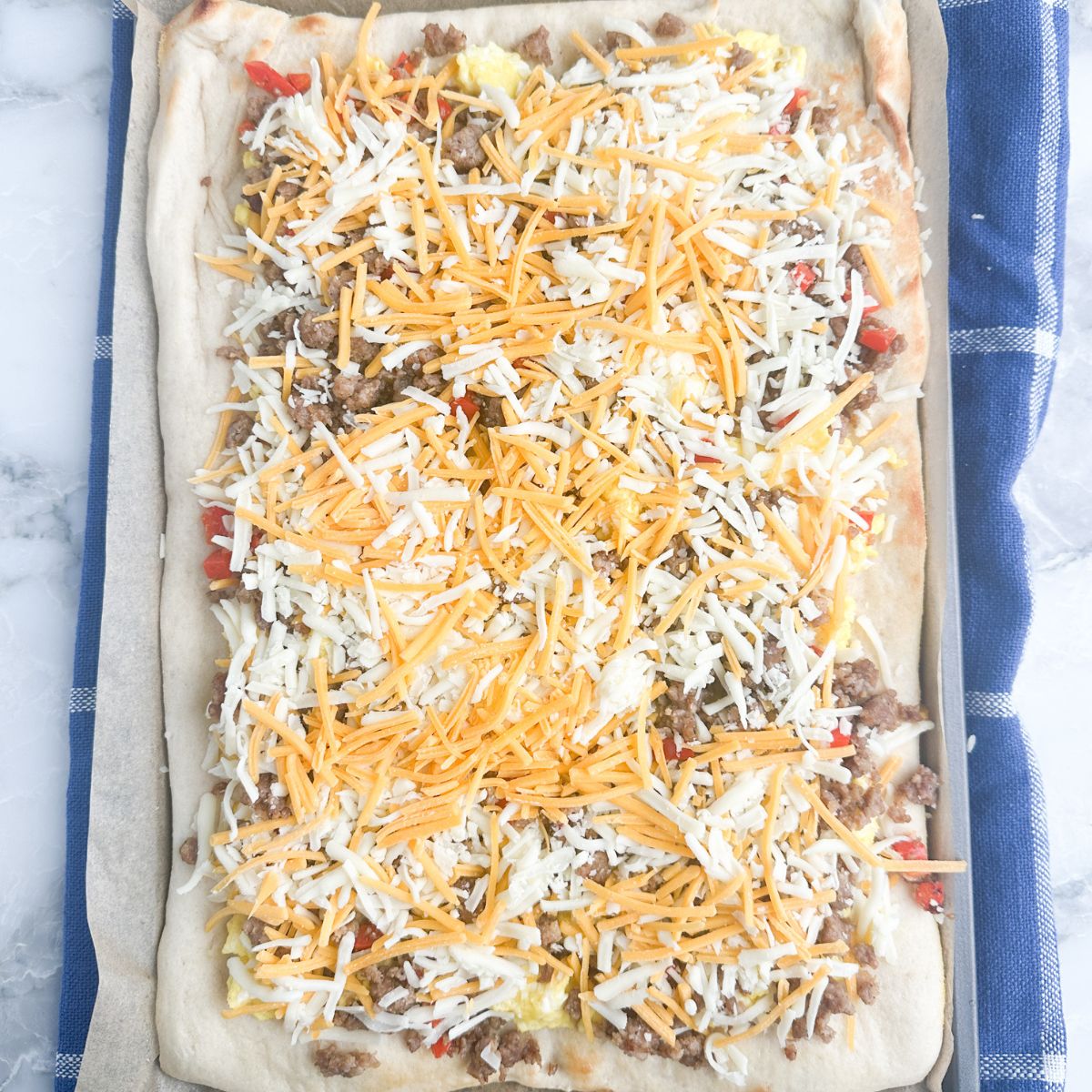 Pizza crust with eggs, sausage, and shredded cheese.