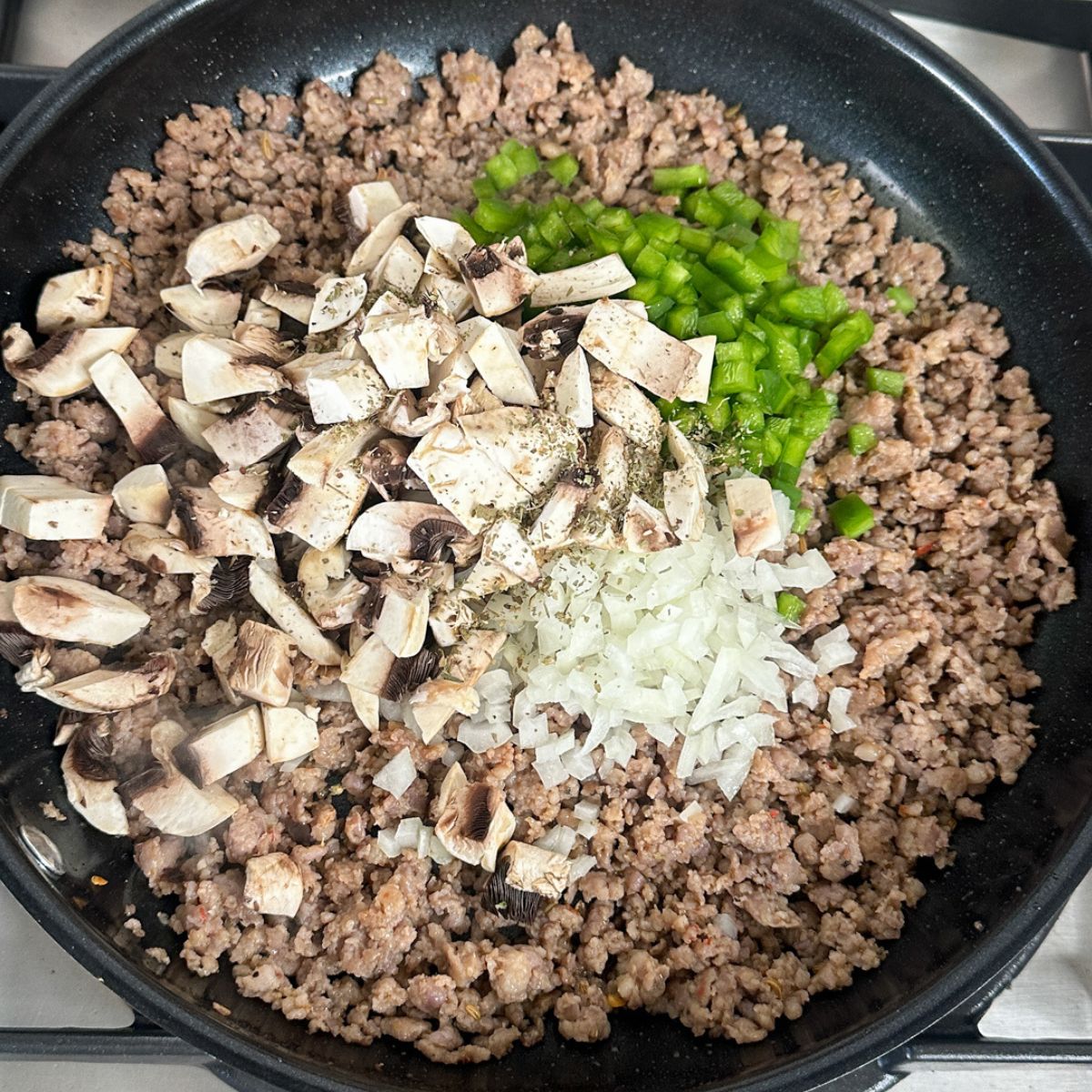 Skillet with cooked and crumbled sausage, mushrooms, onions, and peppers. 