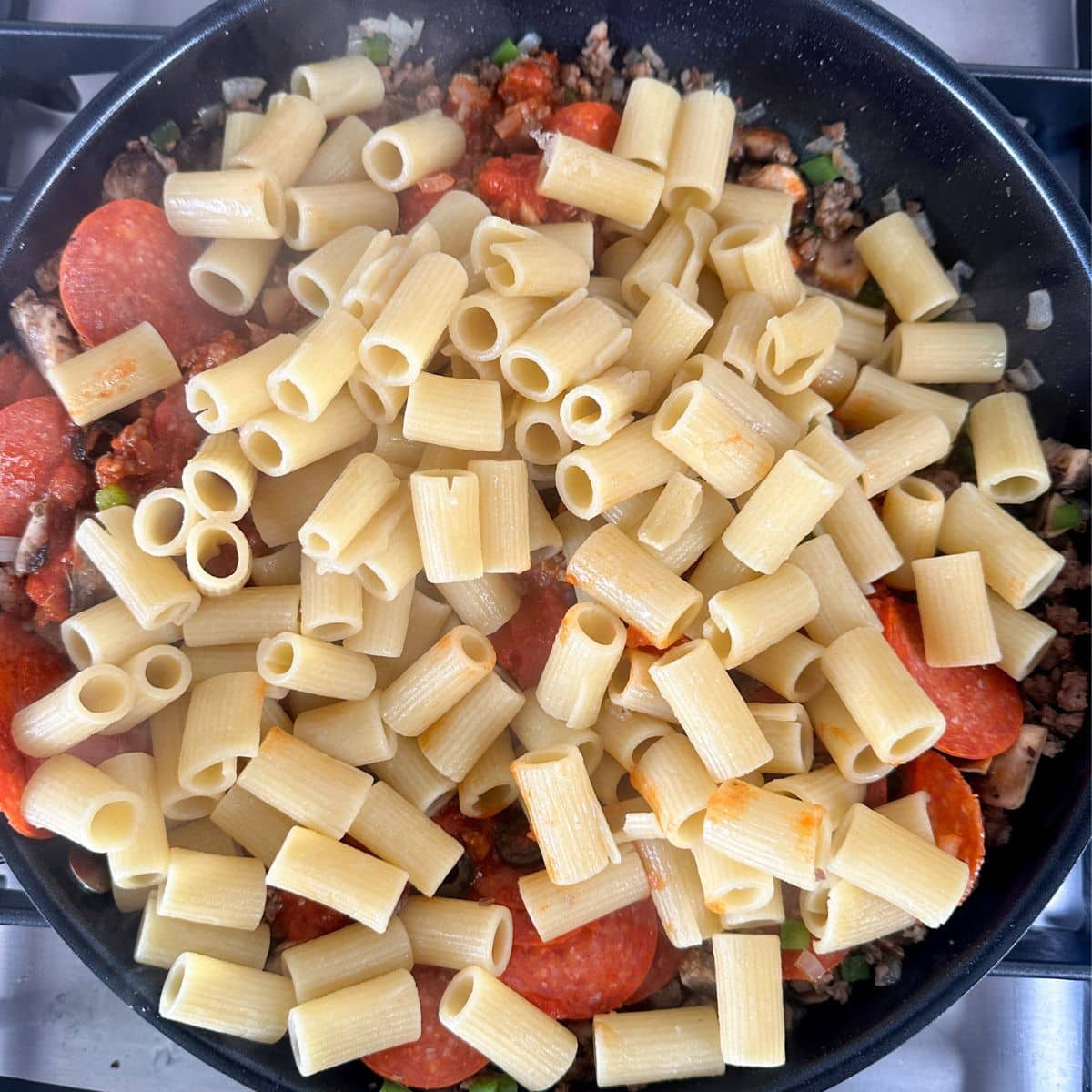 Skillet with sausage, pepperonis, and cooked pasta. 