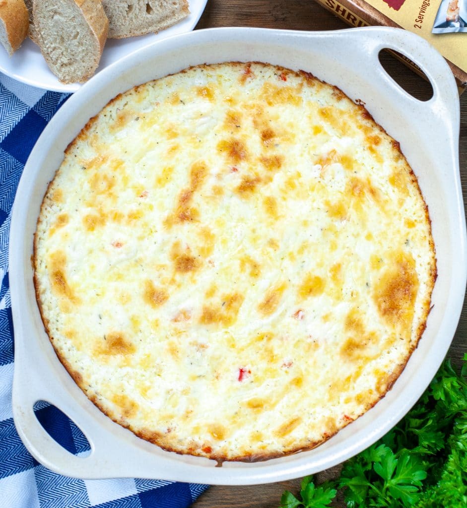 Baking dish filled with shrimp dip. Side plate with bread. 