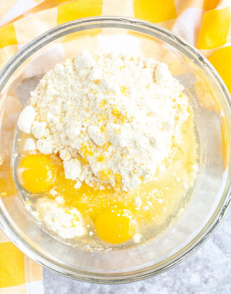 Ingredients for lemon cookies in a glass bowl and yellow checked towel. 