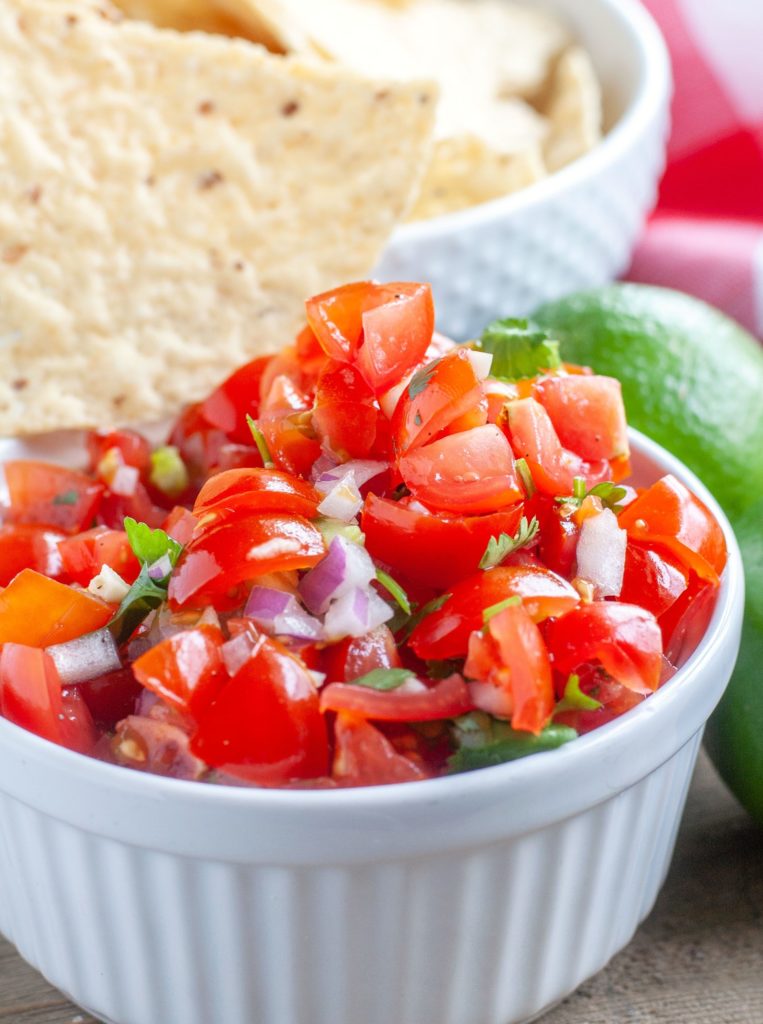 Pico De Gallo In a white bowl with a chip and limes
