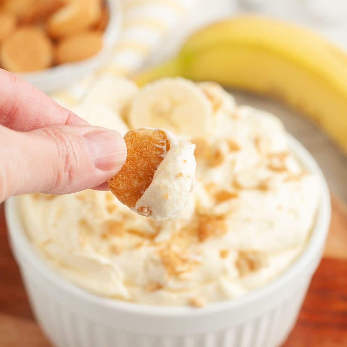 Bowl of banana pudding dip with a cookie being dipped into it. 