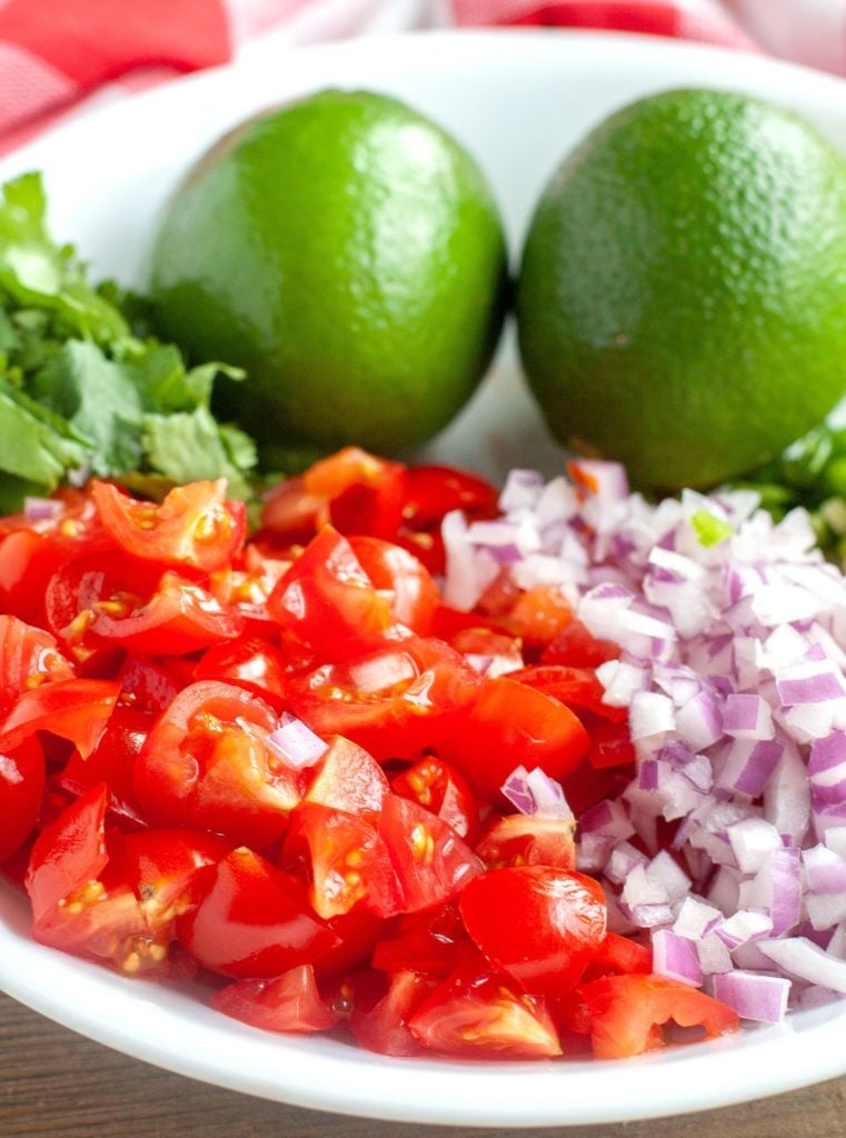 Diced tomatoes, diced red onion, cilantro, 2 limes in a white bowl