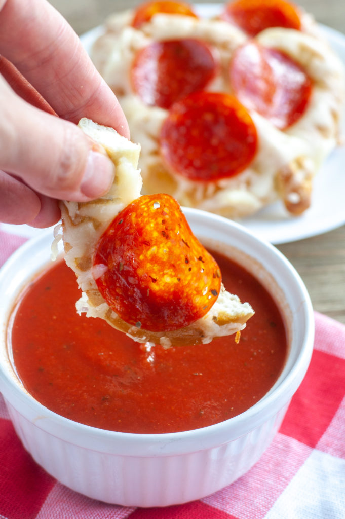 Piece of pepperoni pretzel dipping into marinara sauce. 