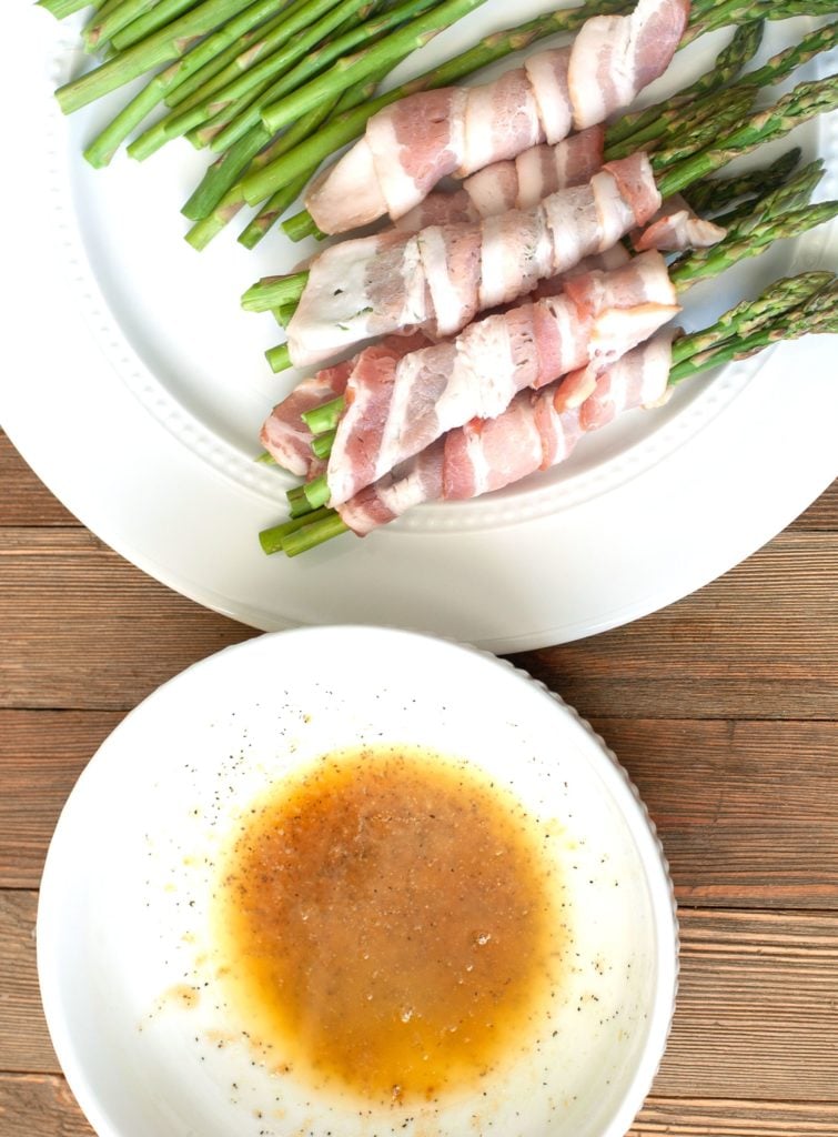 Melted butter and brown sugar in a bowl with bacon wrapped around asparagus